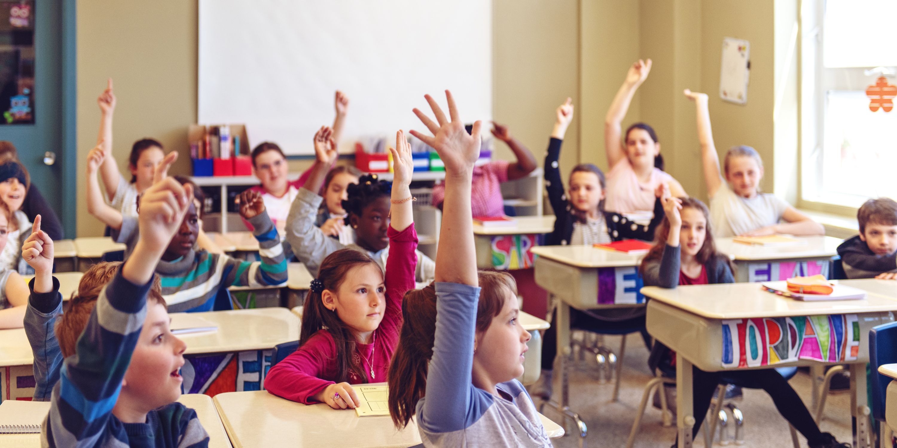students raising hands in a classroom